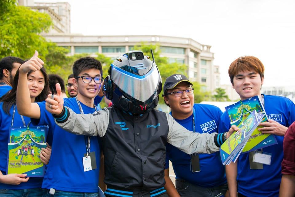 Formula E event photo showing fans posing with a racing helmet, capturing the live audience energy around the electric motorsport campaign.