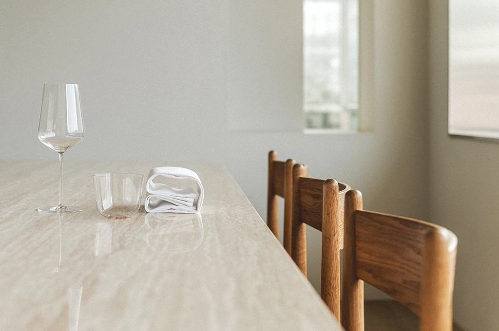대리석 테이블 위에 와인잔과 유리컵, 접힌 냅킨이 놓인 미니멀한 실내 공간