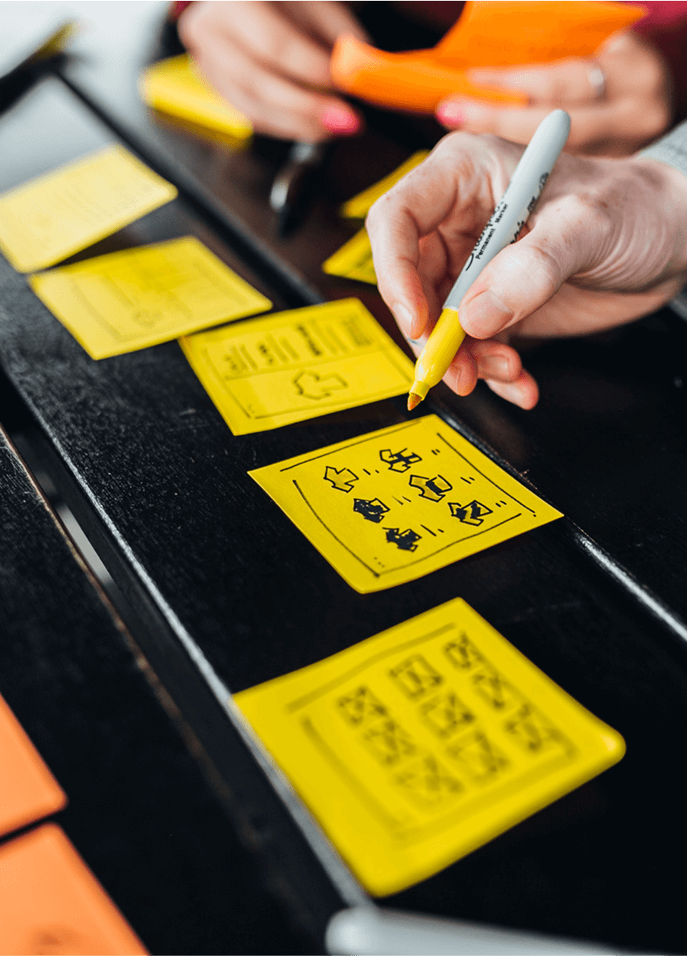 Close-up of hands arranging yellow sticky notes during a design workshop session.