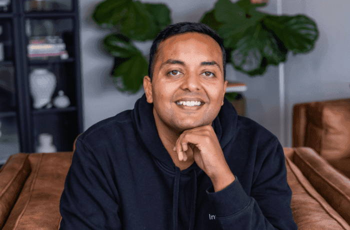 Man in dark hoodie resting chin on hand, smiling.