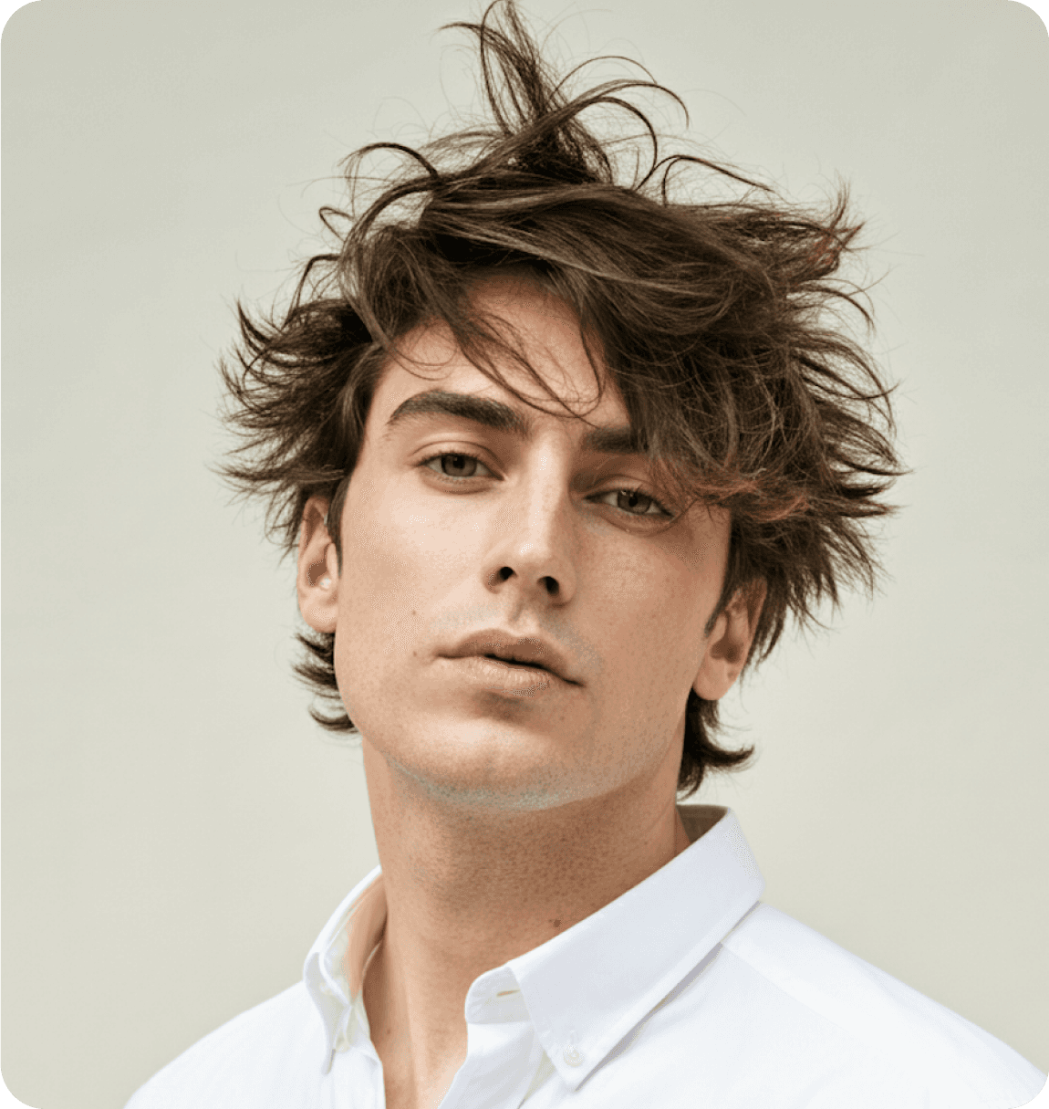 A man with tousled hair, wearing a white shirt, looking directly at the camera.
