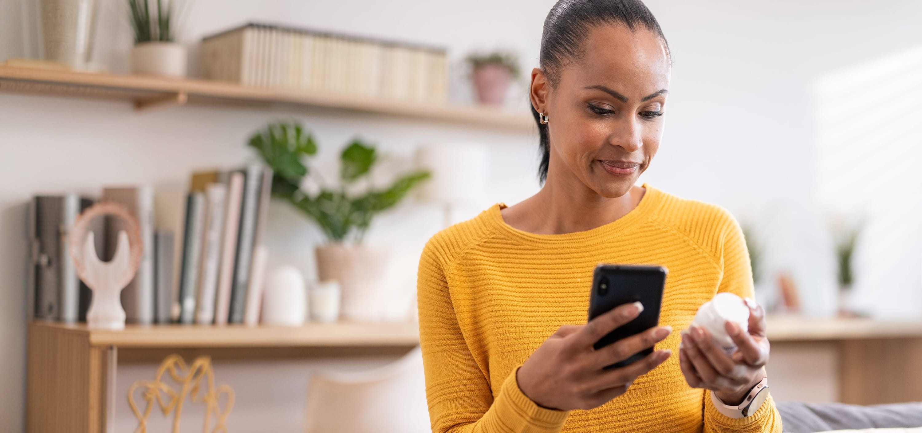 Woman looking at her phone while holding a medication bottle