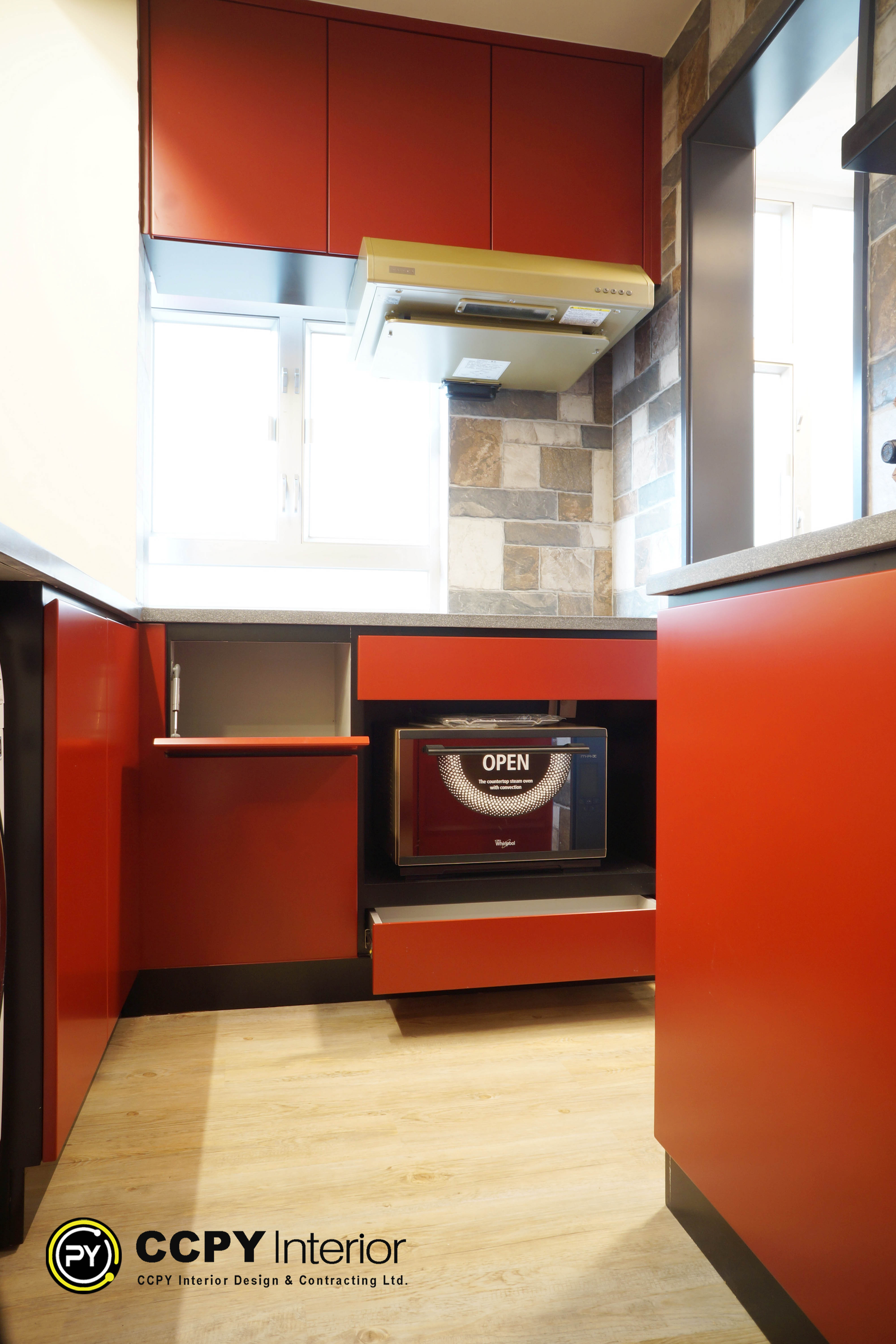 The selected region displays a modern, space-optimized kitchen layout utilizing a bold red and black color scheme.Key Design ElementsBespoke Cabinetry: Vibrant orange-red cabinetry panels with clean, handleless lines to maximize visual flow in a compact layout.Smart Storage: A lift-up cabinet door mechanic is shown, revealing hidden internal shelving above the countertop appliance area.Integrated Appliances: A built-in steam oven or microwave with a digital display labeled "OPEN" is neatly recessed to save counter space.Materials & Backsplash: A rustic, textured stone tile backsplash contrasts against the sleek, glossy kitchen panels.