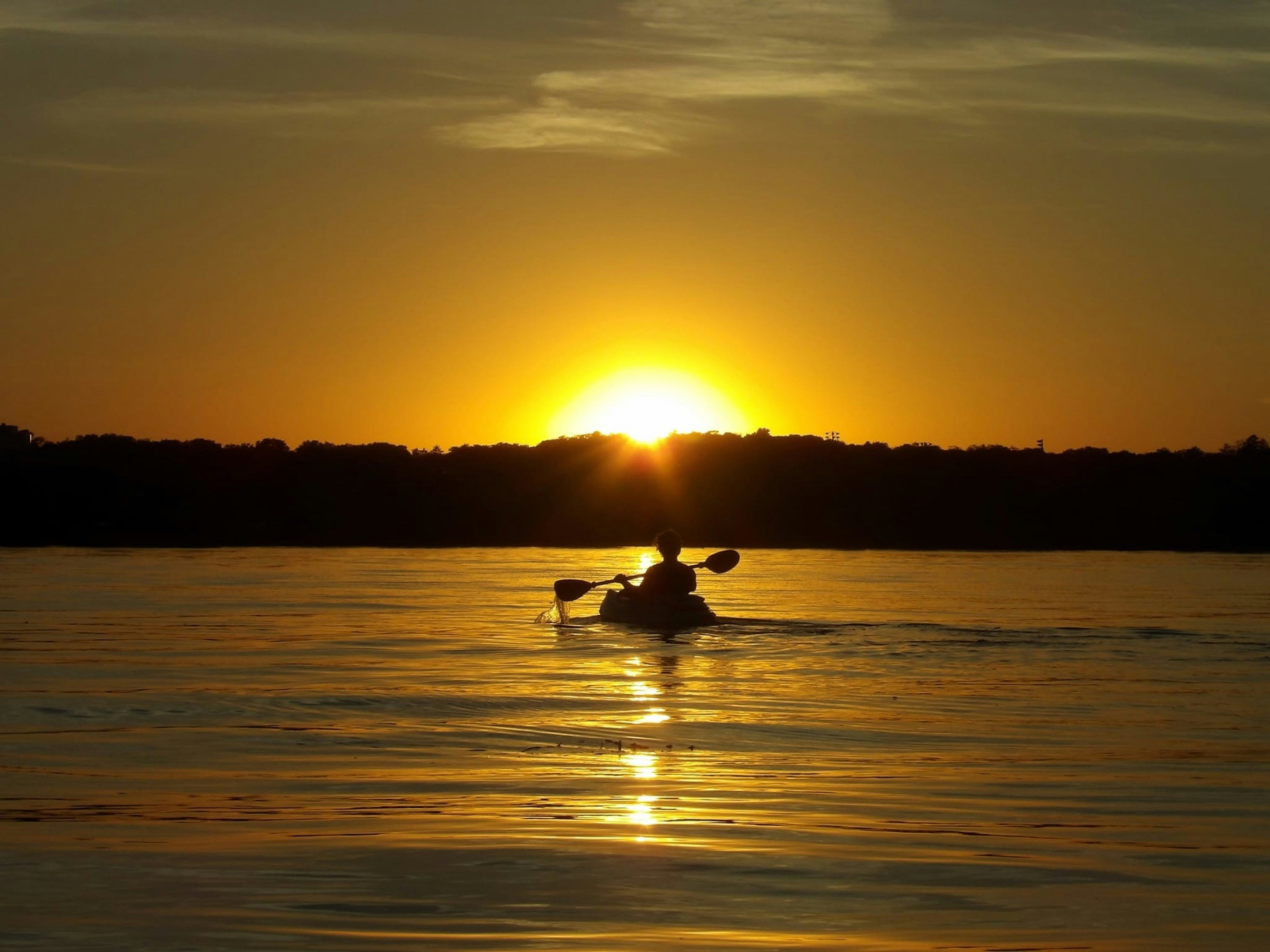 A person on a boat in the water at sunset