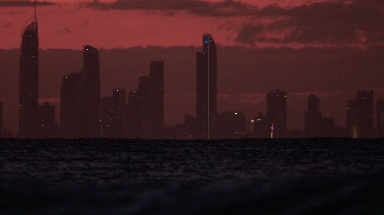 City skyline silhouetted against a dramatic crimson sunset sky over dark water.