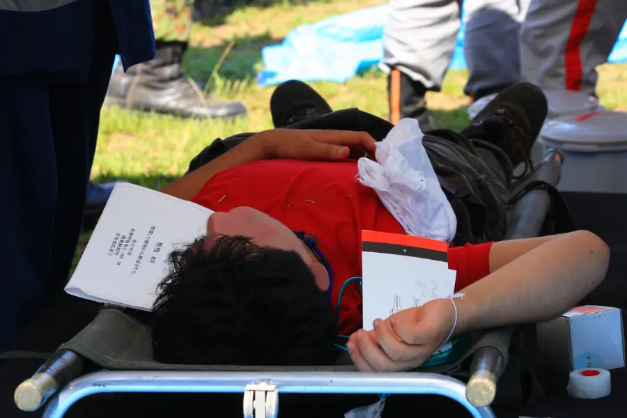 Injured patient lying on a stretcher receiving emergency field triage assessment during an outdoor medical response drill.