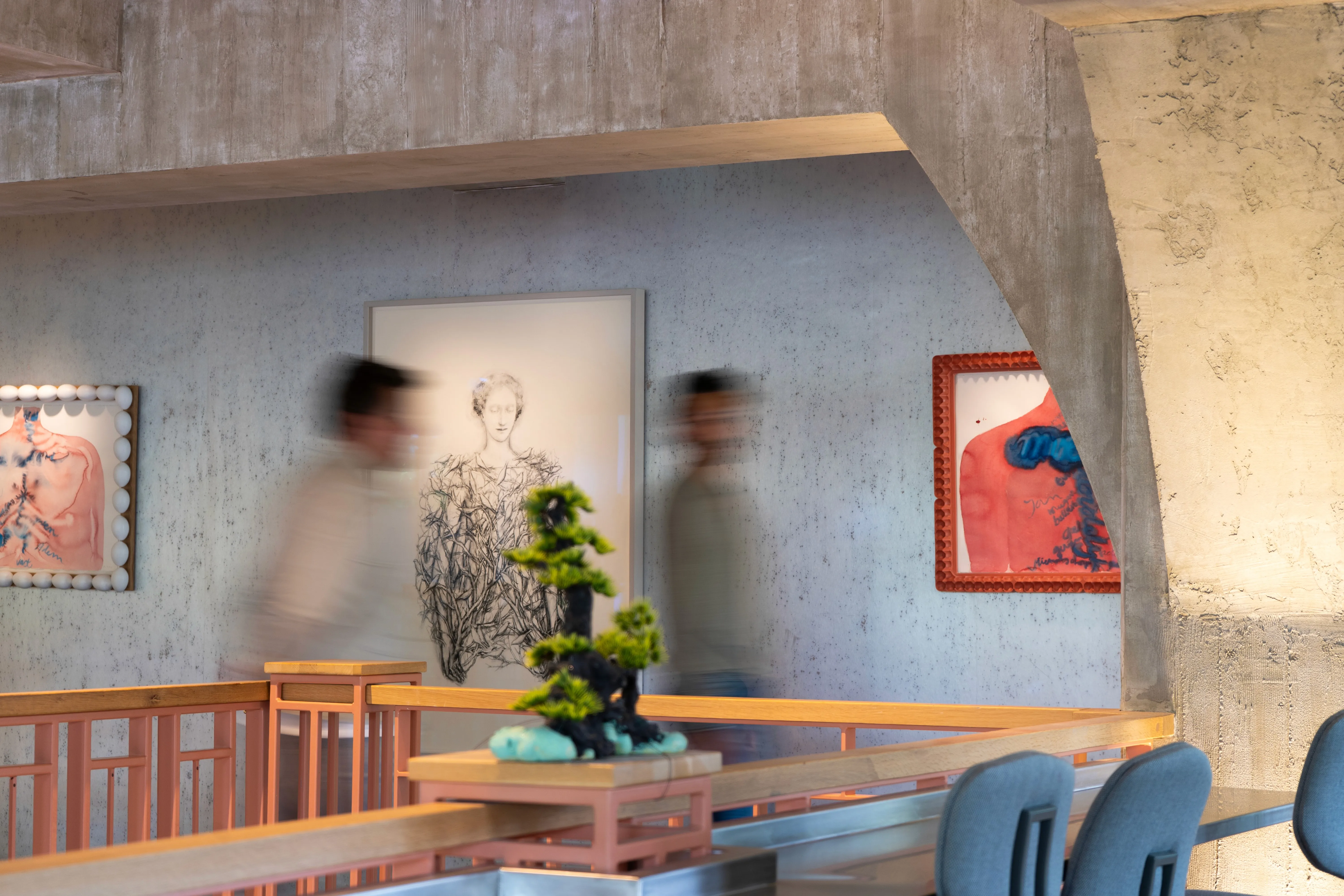 Two individuals stand in a modern interior space featuring artwork on the walls, with a floral arrangement nearby.