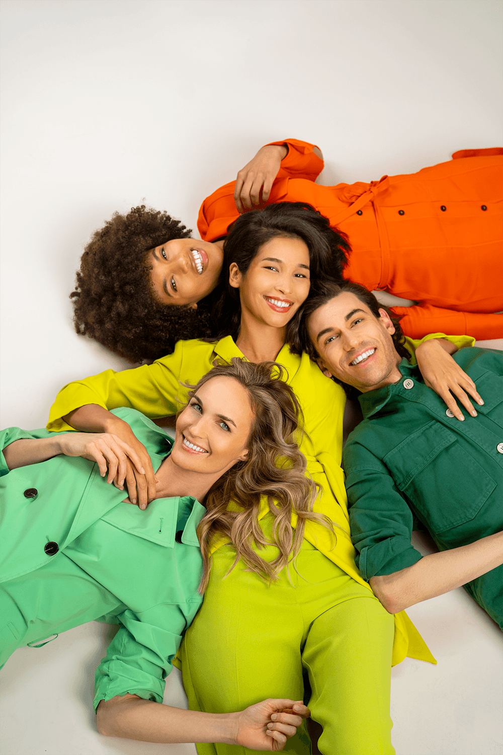 Group portrait of Croma models laying together in colorful outfits, smiling and relaxed indoors