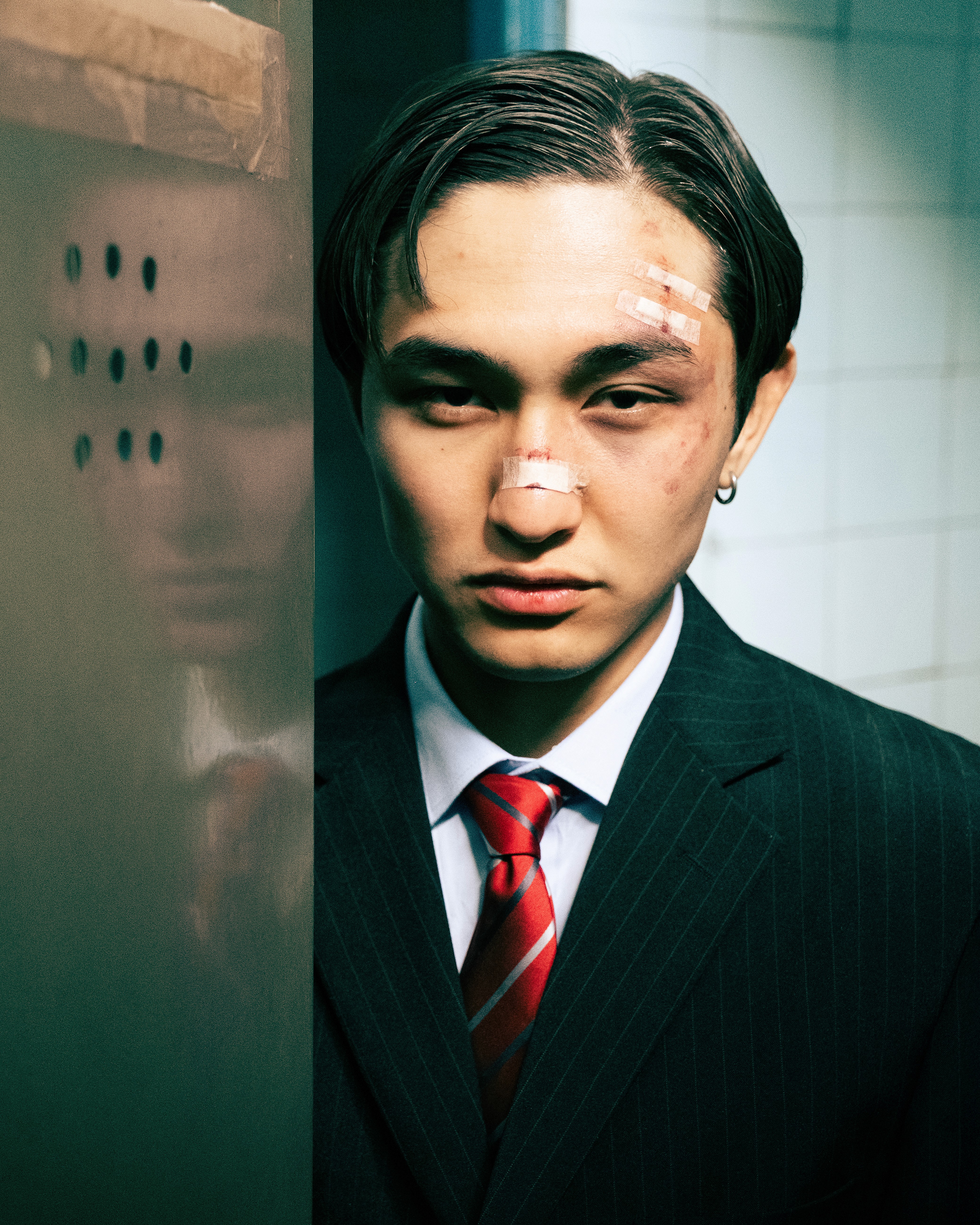 Argen – Loud Silence – head-on portrait next to a reflective surface, with facial bandages and a steady stare