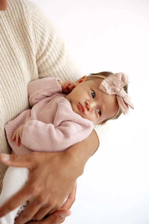 Baby in a pink outfit and headband supported by an adult