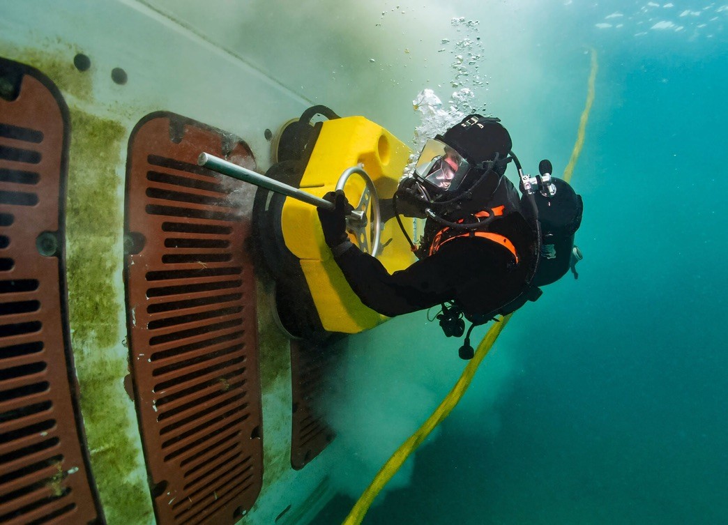 Commercial diver conducting niche-area underwater cleaning on a vessel sea chest using a mechanical tool, illustrating controlled biofouling removal under port and environmental compliance requirements.