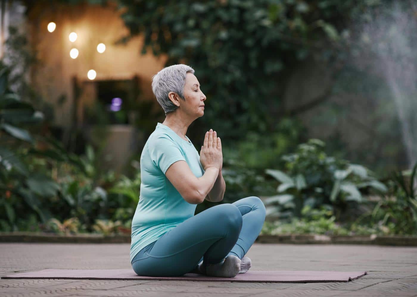 Woman meditating sitting on yoga mat with palms touching in front of her chest