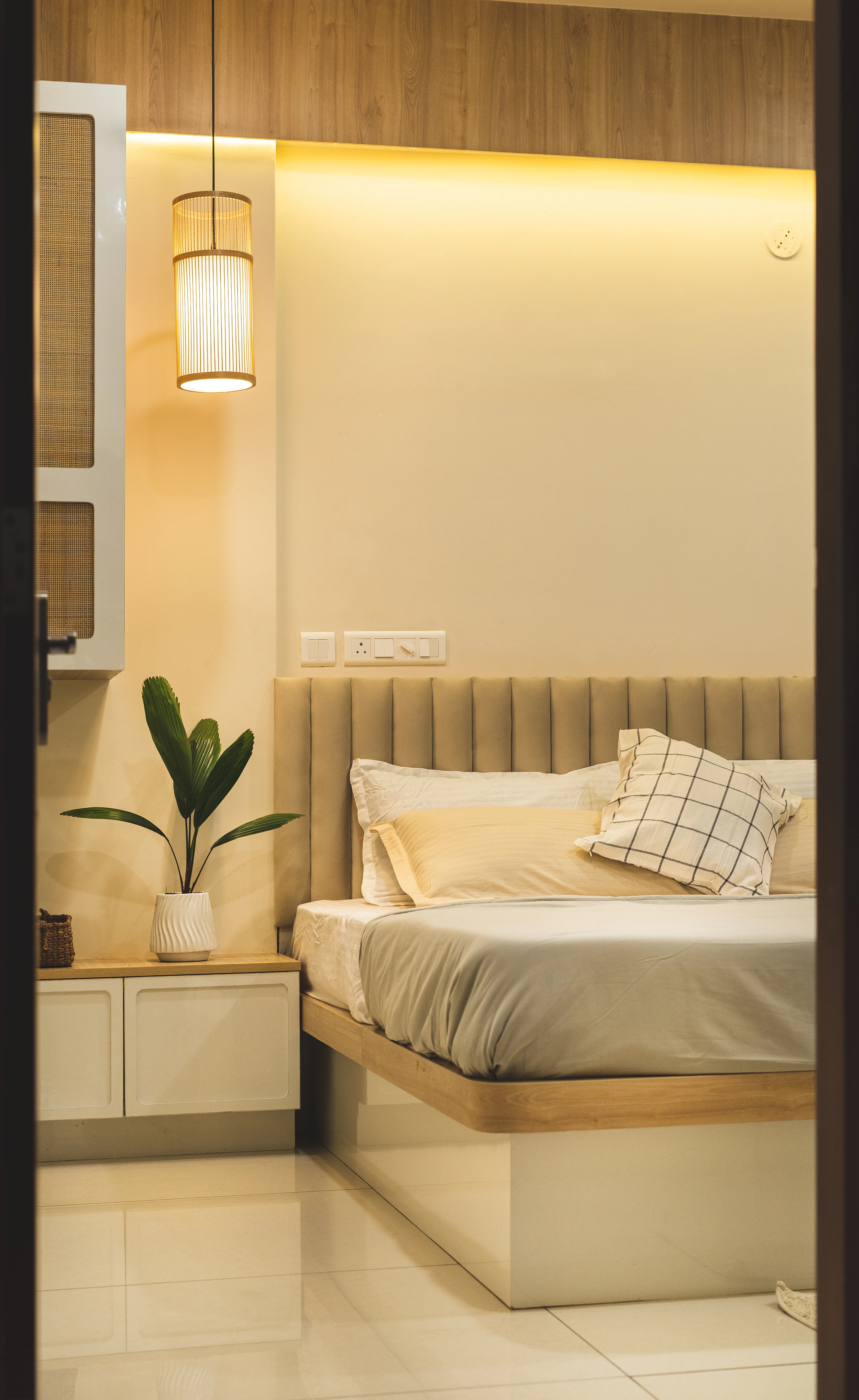 A stylish bedroom featuring a curved bed and a wall-mounted lamp, reflecting minimalistic South Indian design aesthetics.