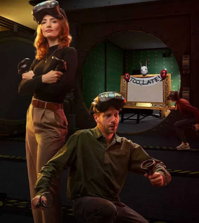A man and a woman in VR gear sneaking through a heist scenario, holding controllers like flashlights near a bank vault entrance.