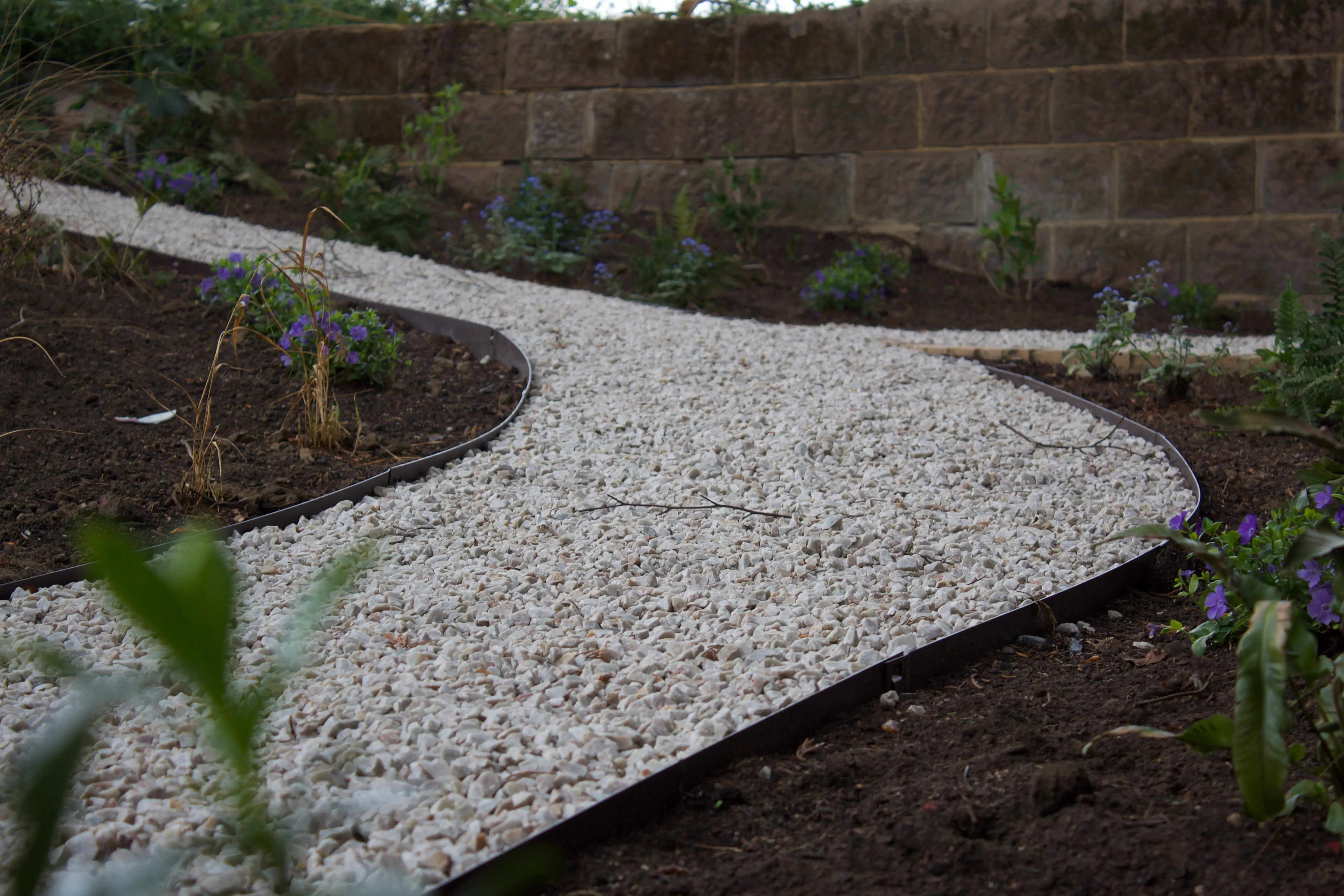A winding stone pathway curves through a garden with green plants, creating a serene outdoor atmosphere.
