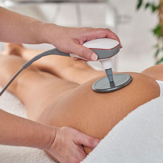 A woman lying down with a towel wrapped around her head, her face glowing with facial oil. She has a peaceful expression, enjoying a skincare treatment.