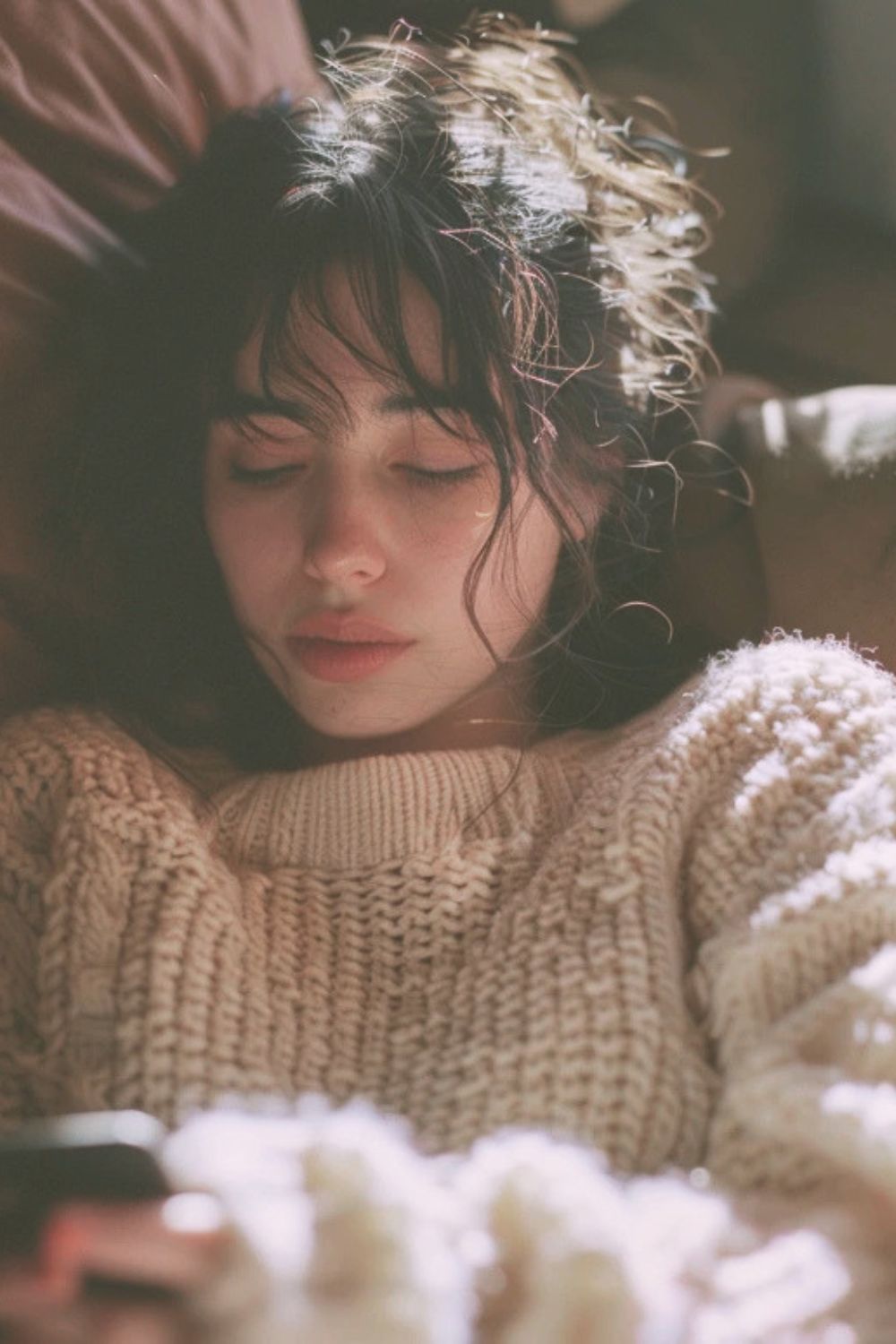 Tired mother resting on a couch with eyes closed, holding her phone after a long postpartum day