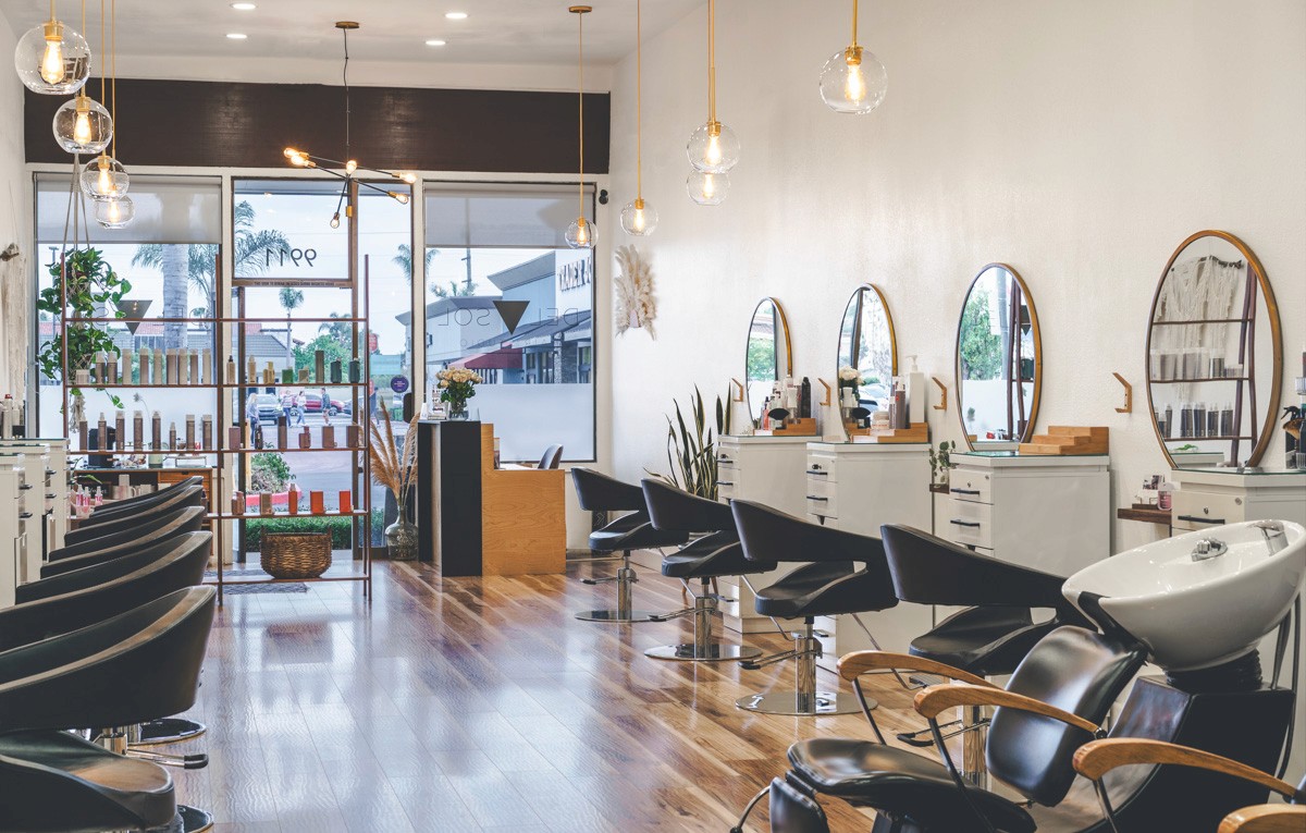 Interior of Del Sol Hair Studio in Huntington Beach, featuring a bright, modern salon with sleek styling stations, large round mirrors, natural light, and warm wood flooring—used as the hero image on the homepage.