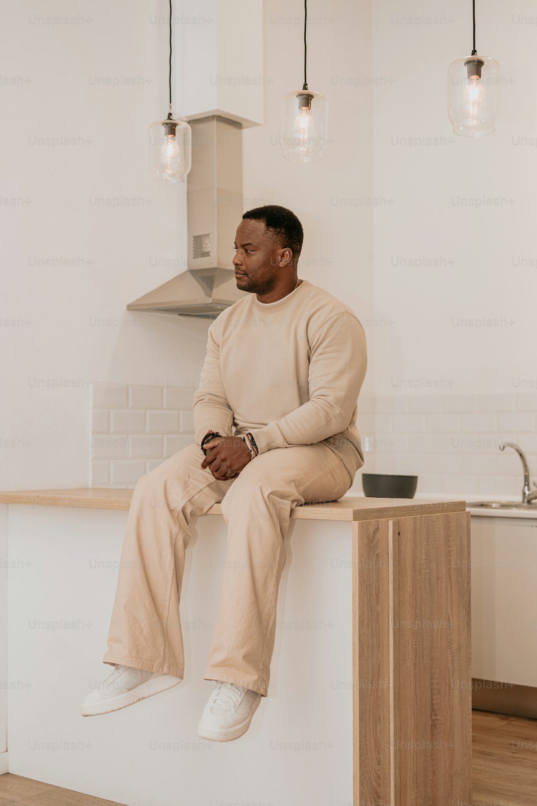 Homme assis sur un comptoir de cuisine moderne, style minimaliste, intérieur lumineux.