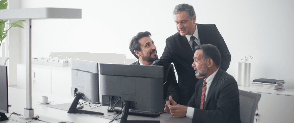 Three men in suits in front of a computer at work