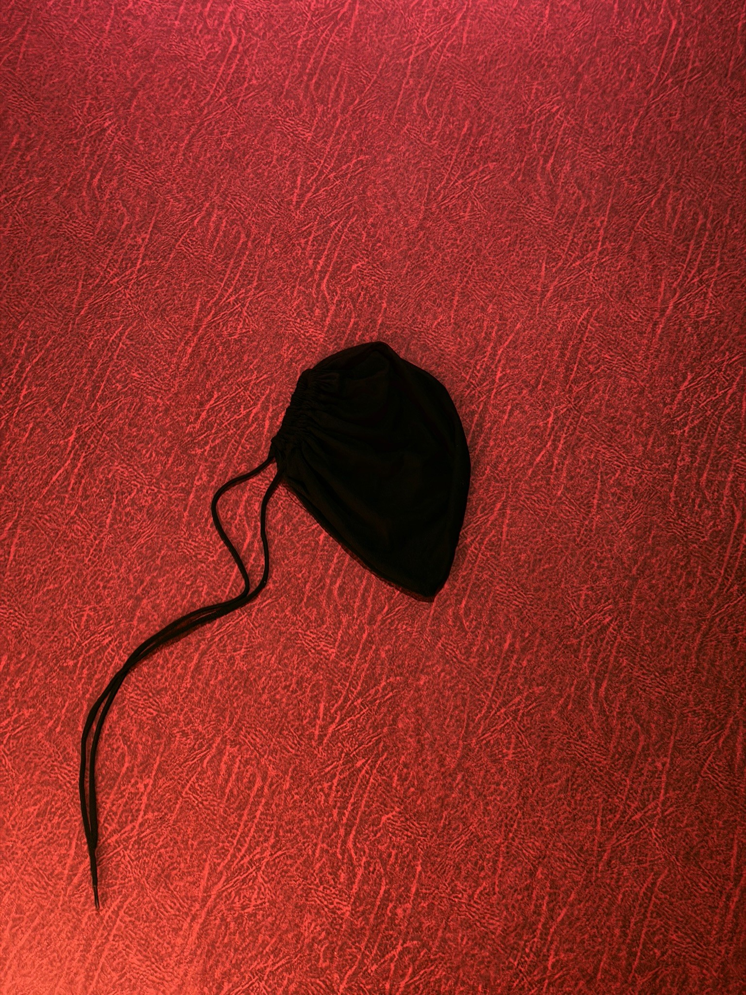 A small, black drawstring pouch against a reddish textured backdrop, possibly a jewelry bag or small gift bag.