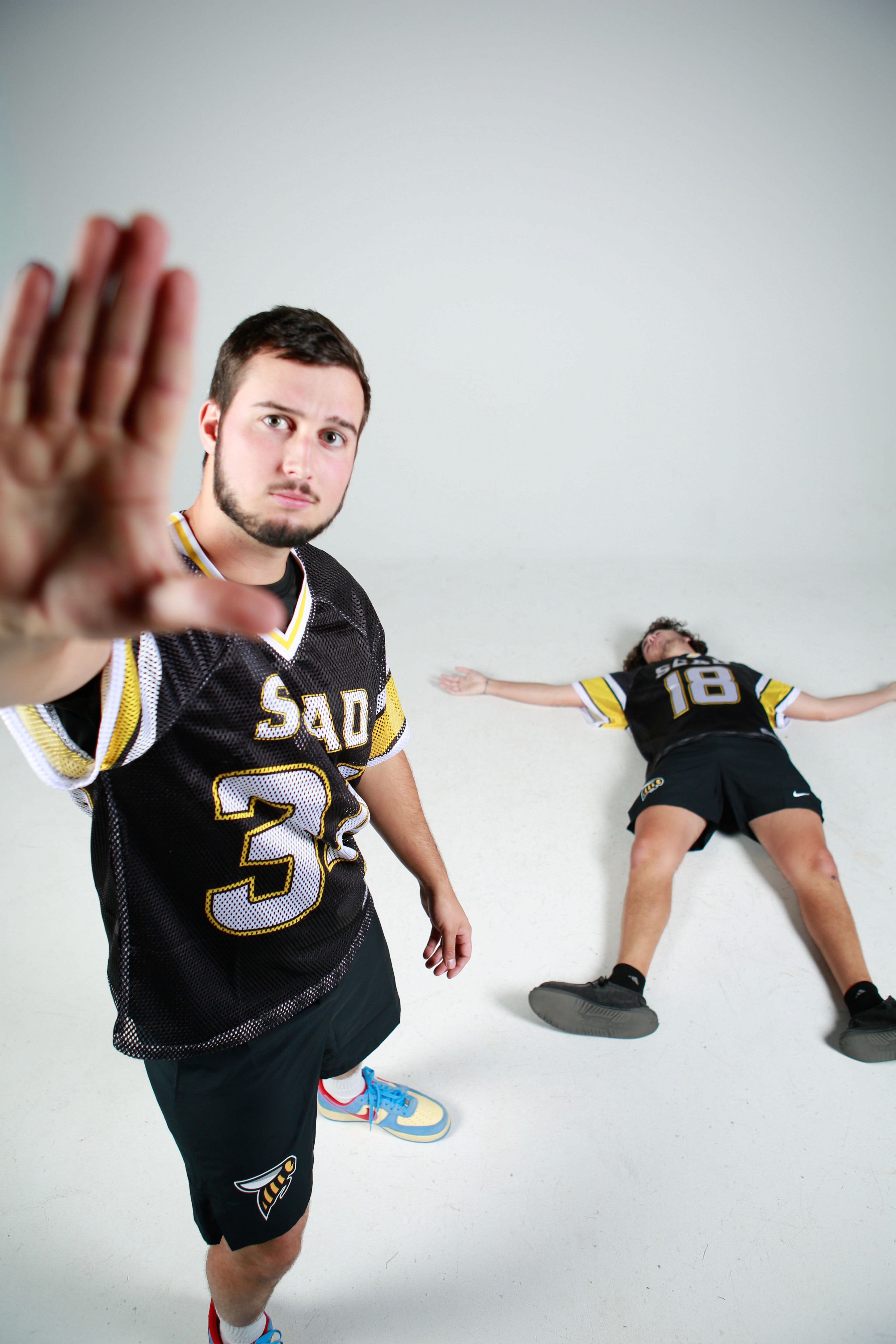 A person posing in a lacrosse social media day shoot with a teamate laying on the ground 