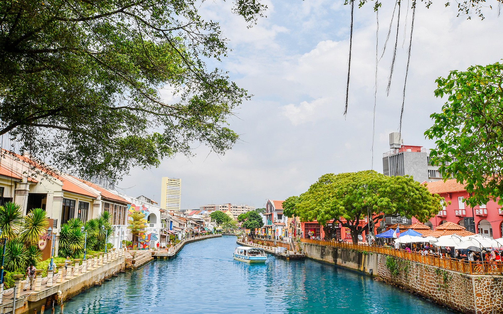 Melaka River with colorful buildings and a boat, part of the Historical Melaka Tour from Kuala Lumpur.