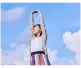 Persona joven estirándose con los brazos hacia arriba bajo un cielo azul con nubes.