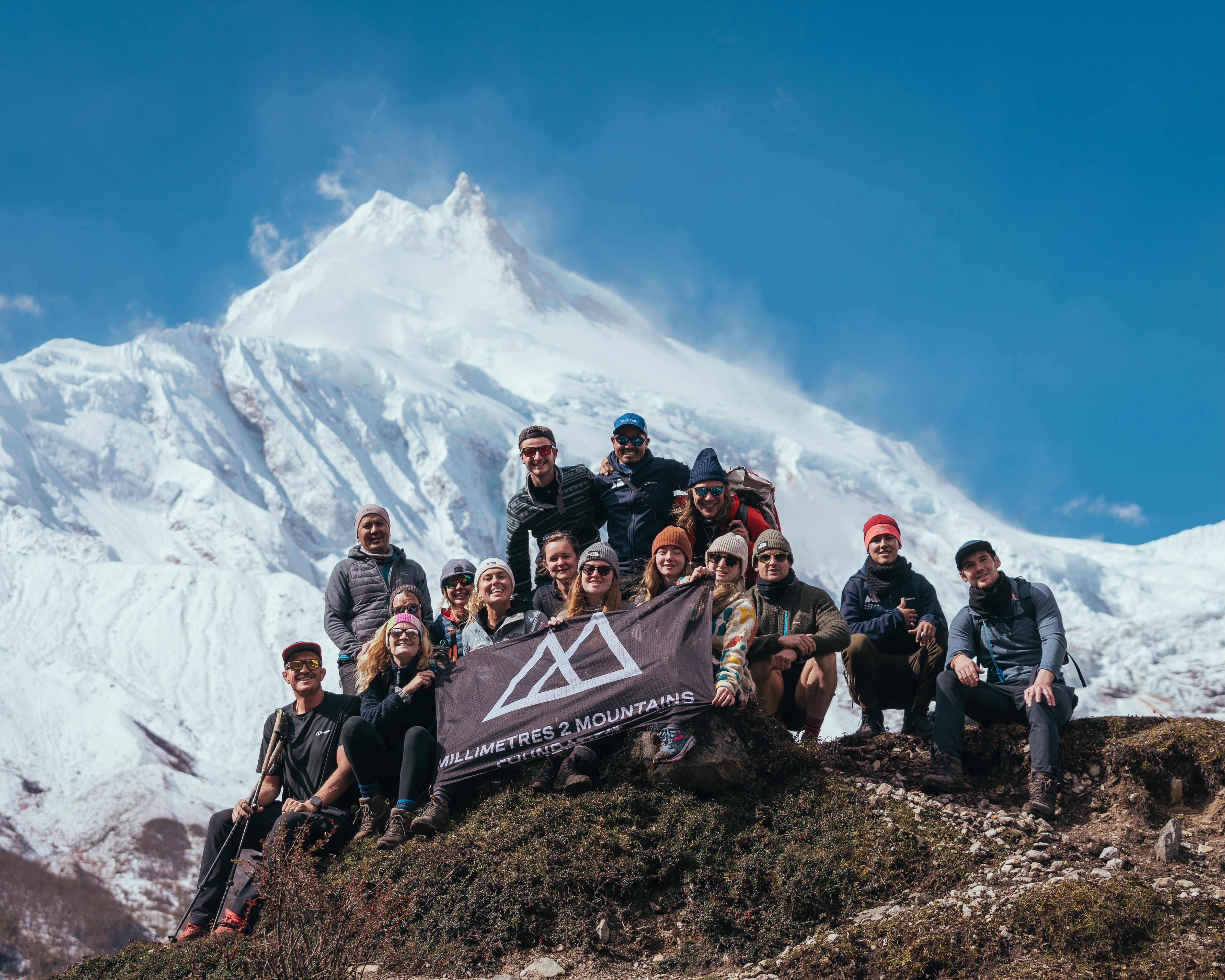 Millimetres 2 Mountains expedition group holding the foundation flag beneath a snow-covered Himalayan peak