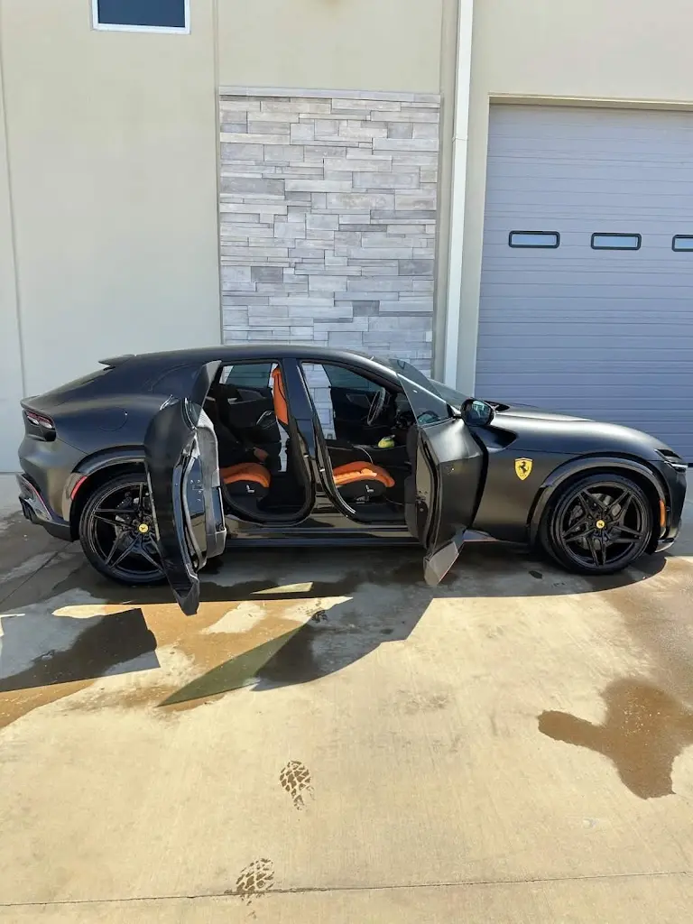 A dark blue Hyundai Sonata receiving a professional mobile car wash in a Houston driveway with soap suds visible on the ground.