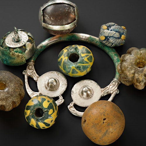 A collection of vintage beads and ornaments with intricate designs, some metallic and others made from stone, arranged on a dark surface.