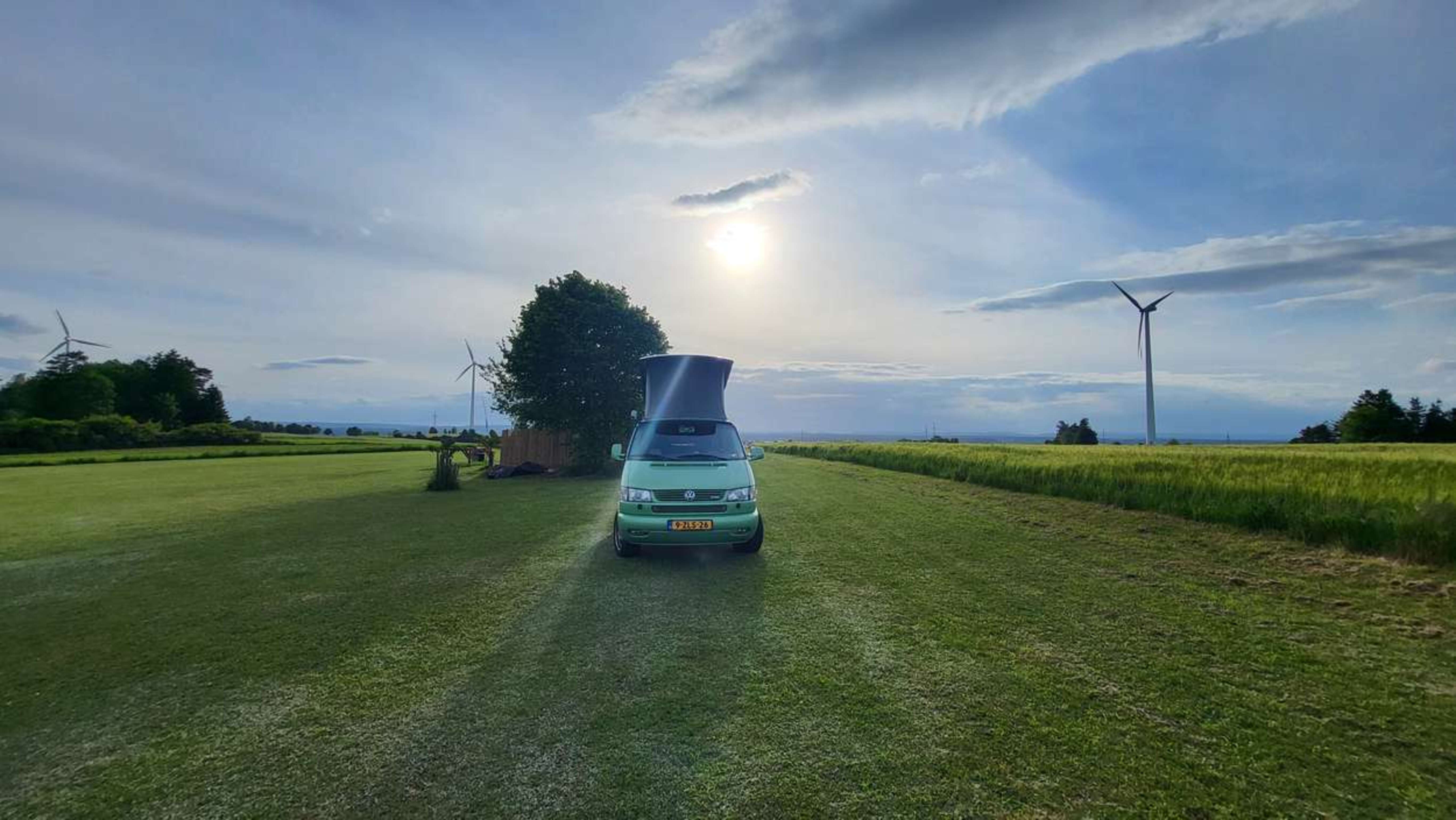 A campervan parked in a wide grassy field with windmills in the background.