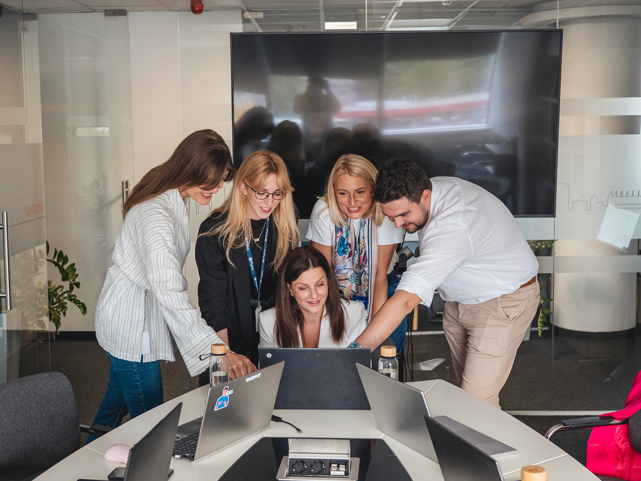 Group of colleagues gathered around a desk looking at a laptop during a team discussion.