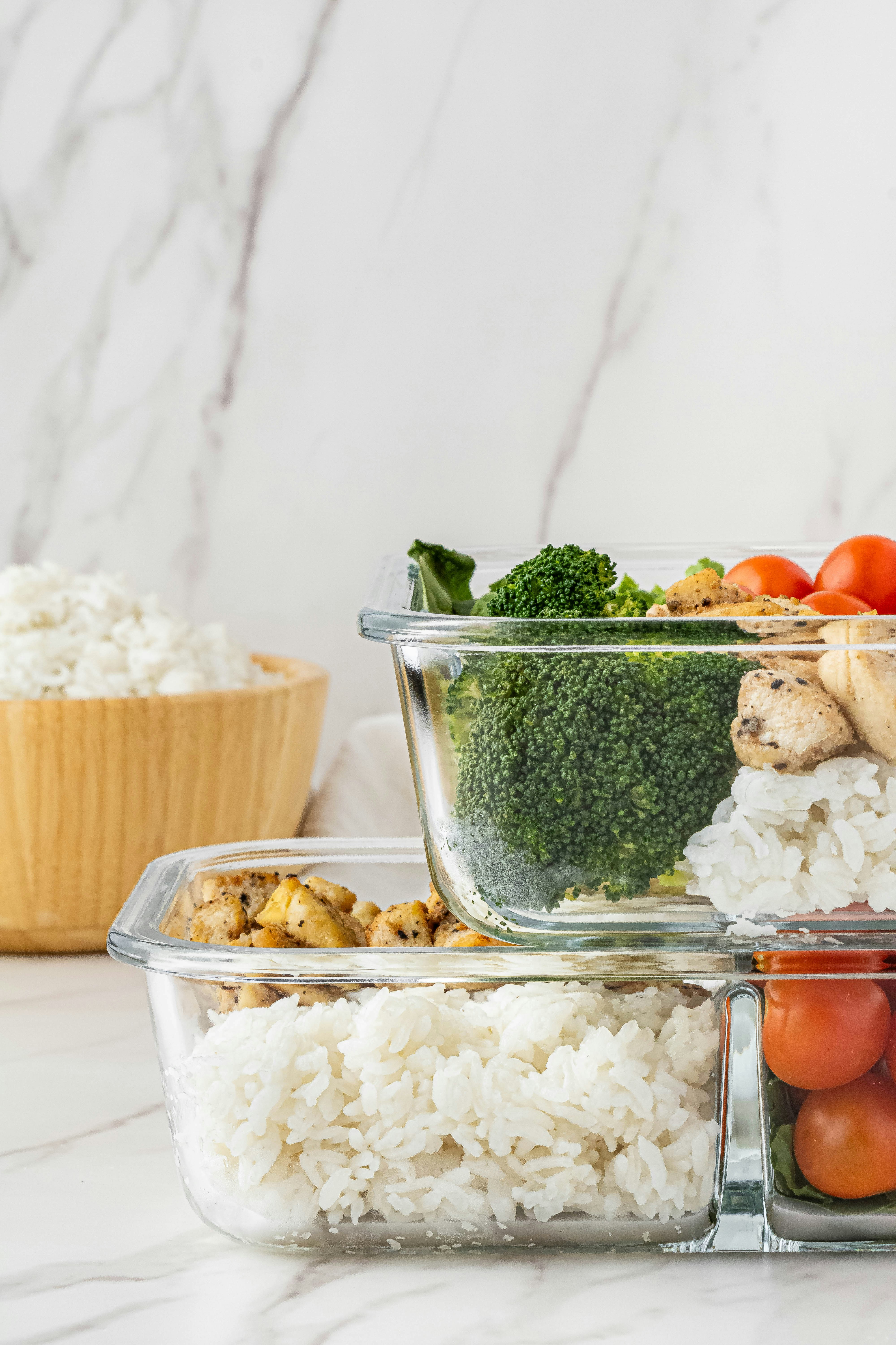 Glass meal prep containers with rice, chicken, broccoli, and cherry tomatoes.