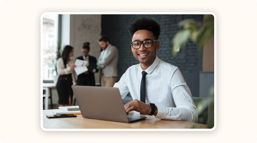 A young entrepreneur smiling while working on a laptop, representing outsourced logistics to grow ecommerce with peace of mind.
