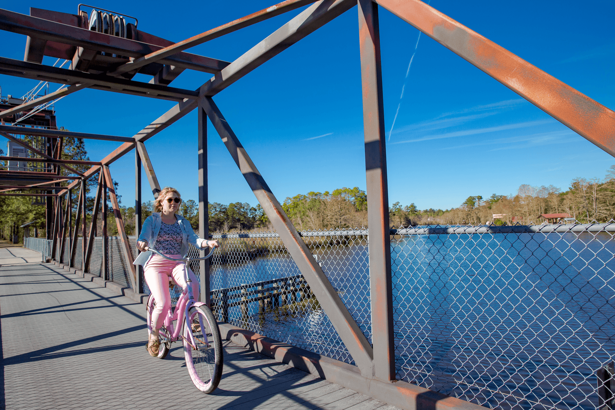 Woman on a pink bicycle riding along the waterfront on The Tammany Trace in Mandeville Louisiana