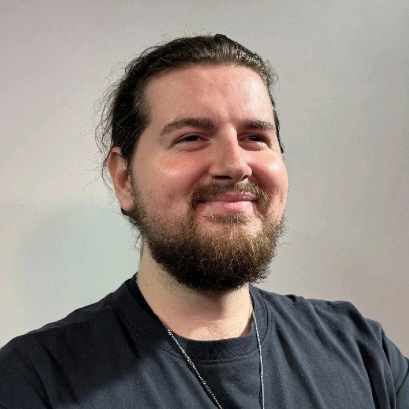 Portrait of Jake Carter, a young man with short dark hair wearing a white shirt and earphones, looking slightly upward against a neutral background.