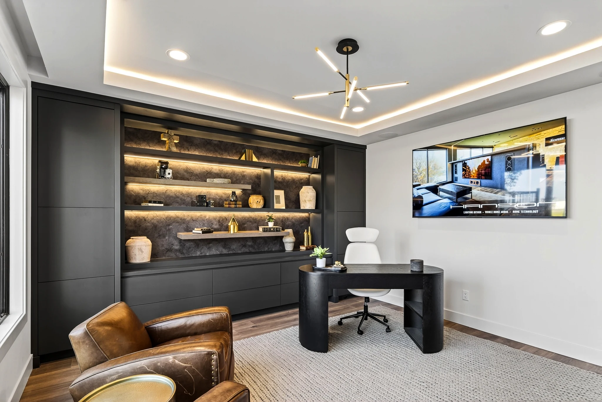 Home office at Three Oaks with a desk, leather chairs and illuminated dark built-in shelving