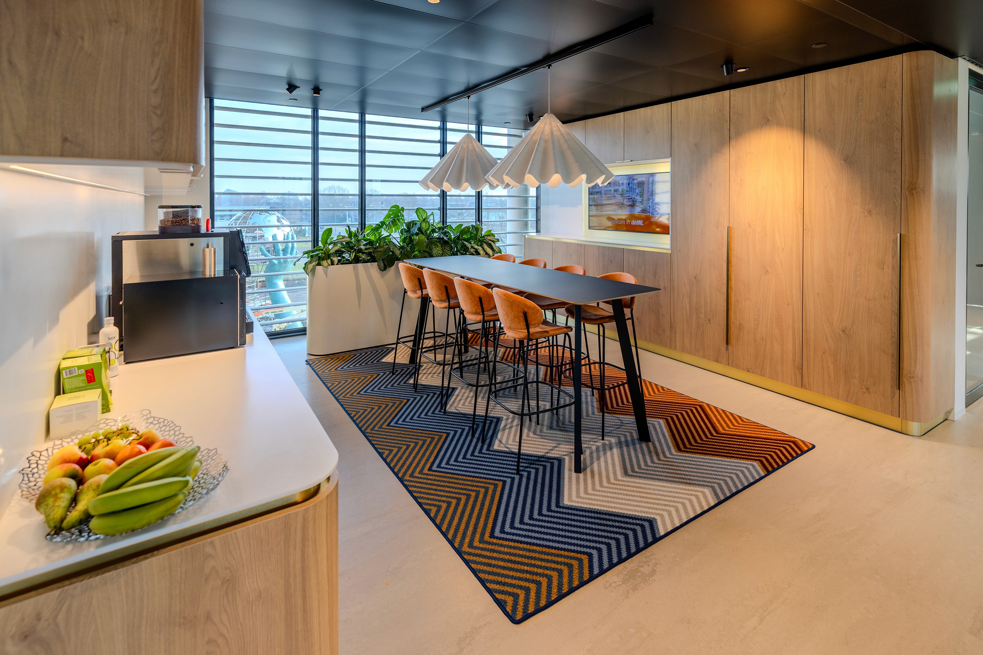 Moderne pantry met donkerhouten wandkast, oranje barkrukken en keukenwerkblad, verlicht door een minimalistische hanglamp – AFAS DotNL, DSN Workspace Solutions