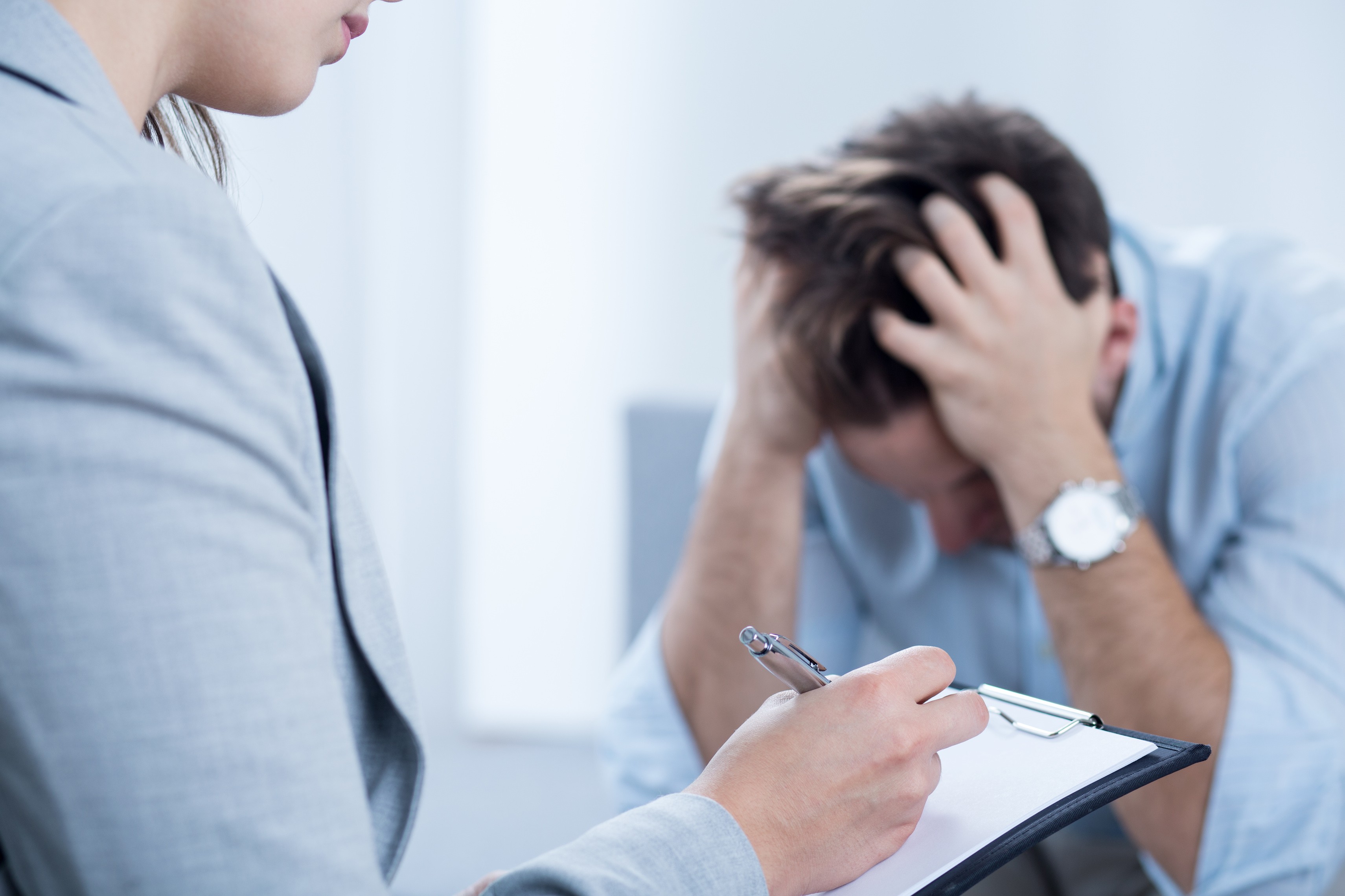 Mann greift sich verzweifelt auf den Kopf, Coachin schreibt auf Block Noitzen mit