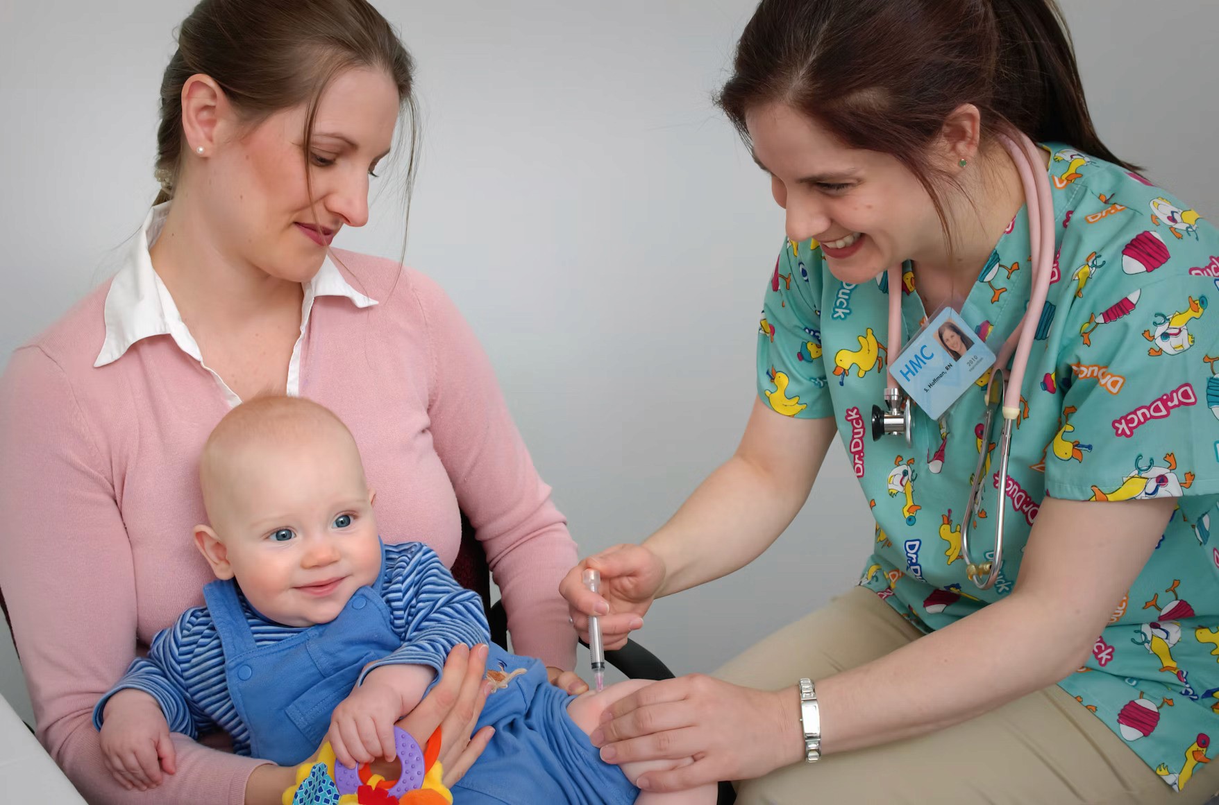 Baby receiving vaccination from nurse while sitting on mother's lap in a healthcare setting.