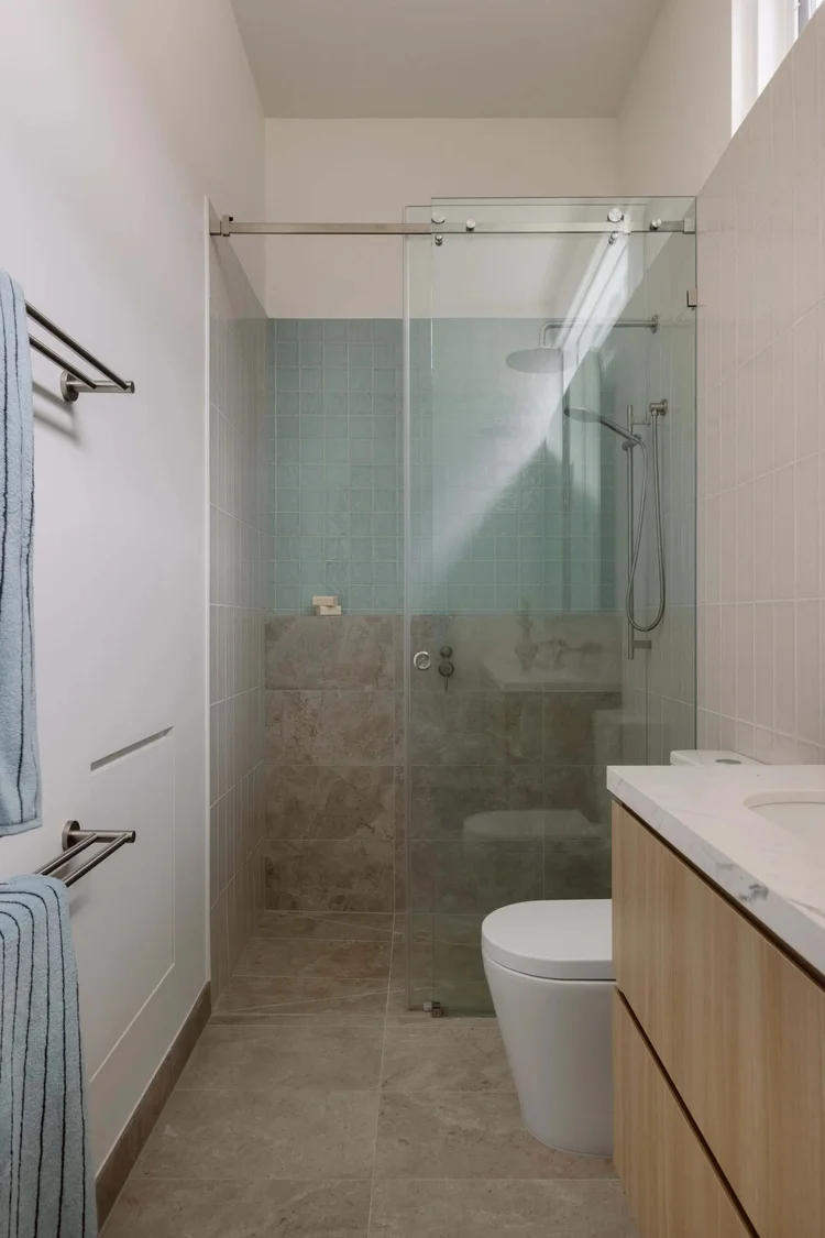 Modern bathroom with glass shower, sleek tiles, and wooden vanity.