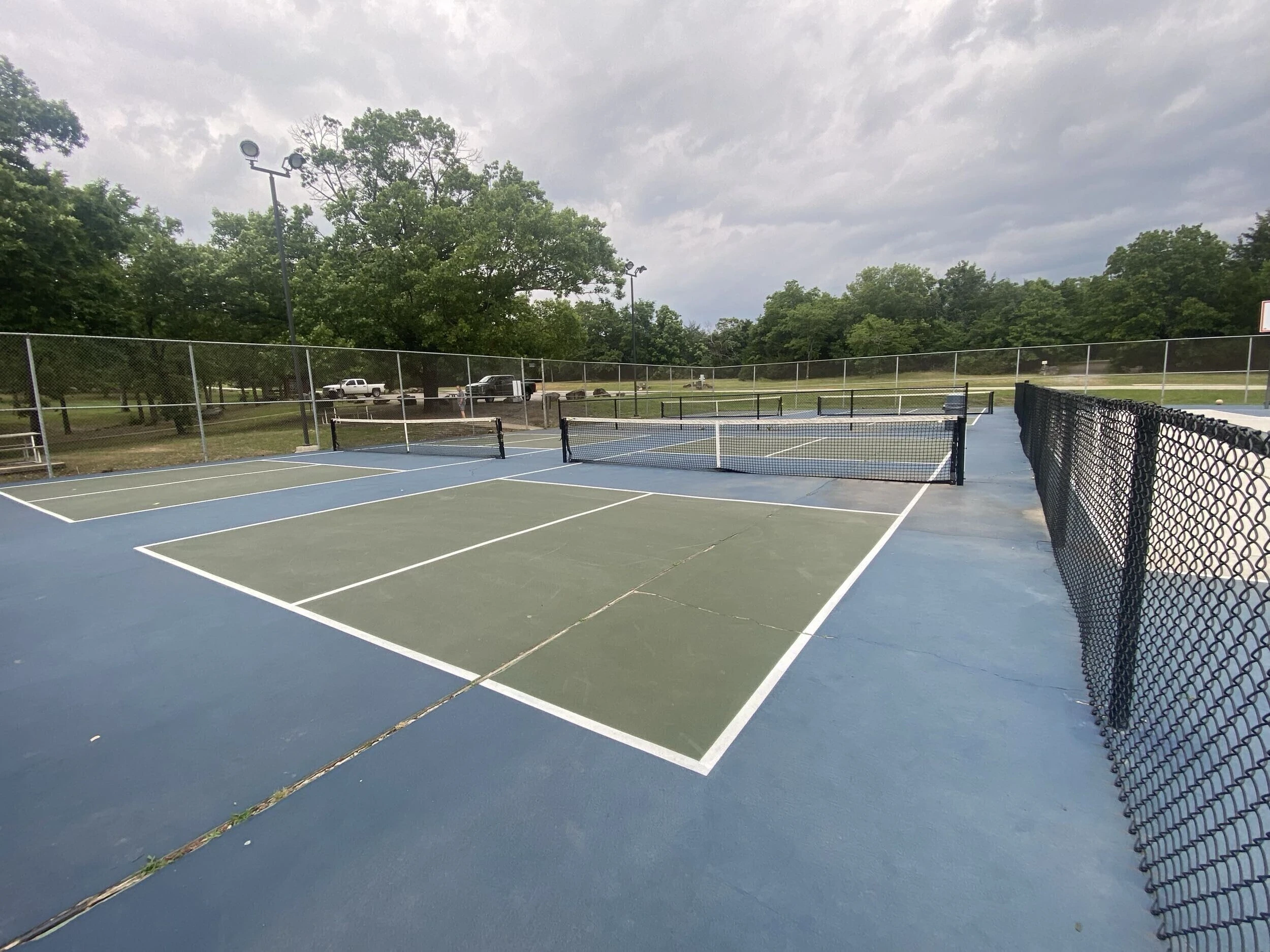 Faded green and blue pickleball courts with visible cracking before resurfacing at Bell Park in Greenwood, AR