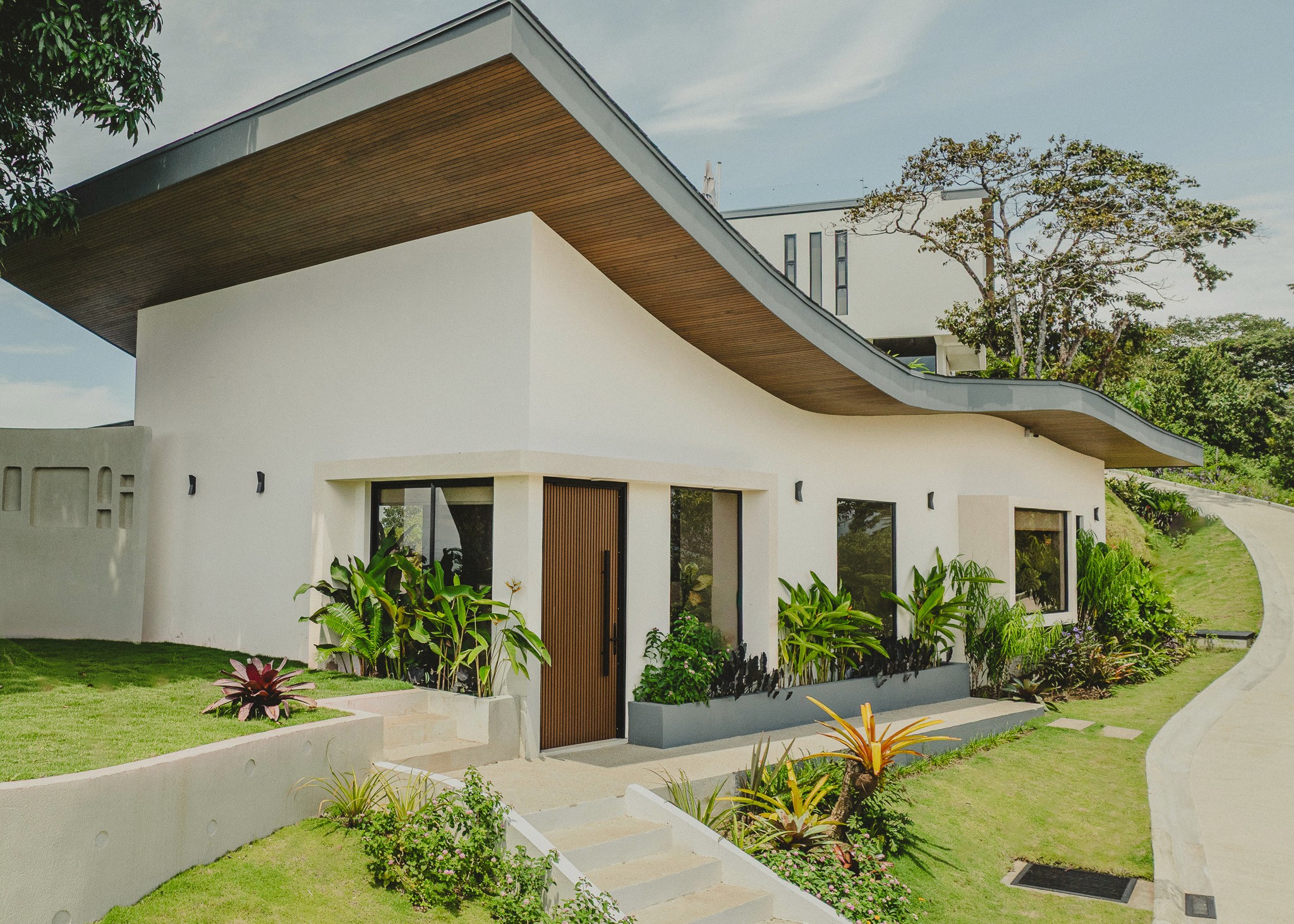 Exterior of a modern Costa Rica luxury villa featuring a distinctive wavy roofline, white architecture, and landscaped tropical gardens.