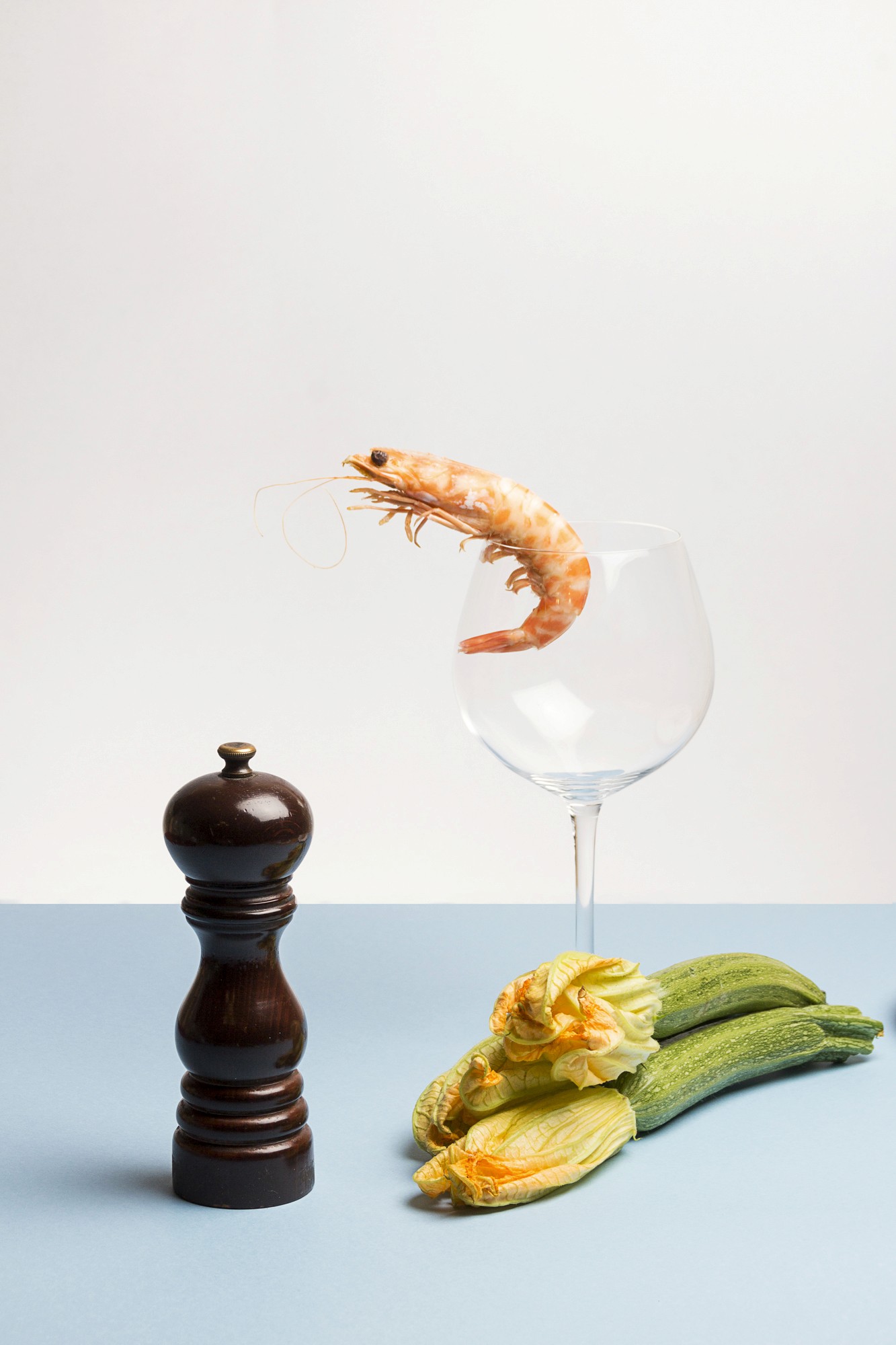 Nature morte d'ingrédients composant un plat contenant des crevettes et du safran et du poivre sur un table au fond bleu ciel