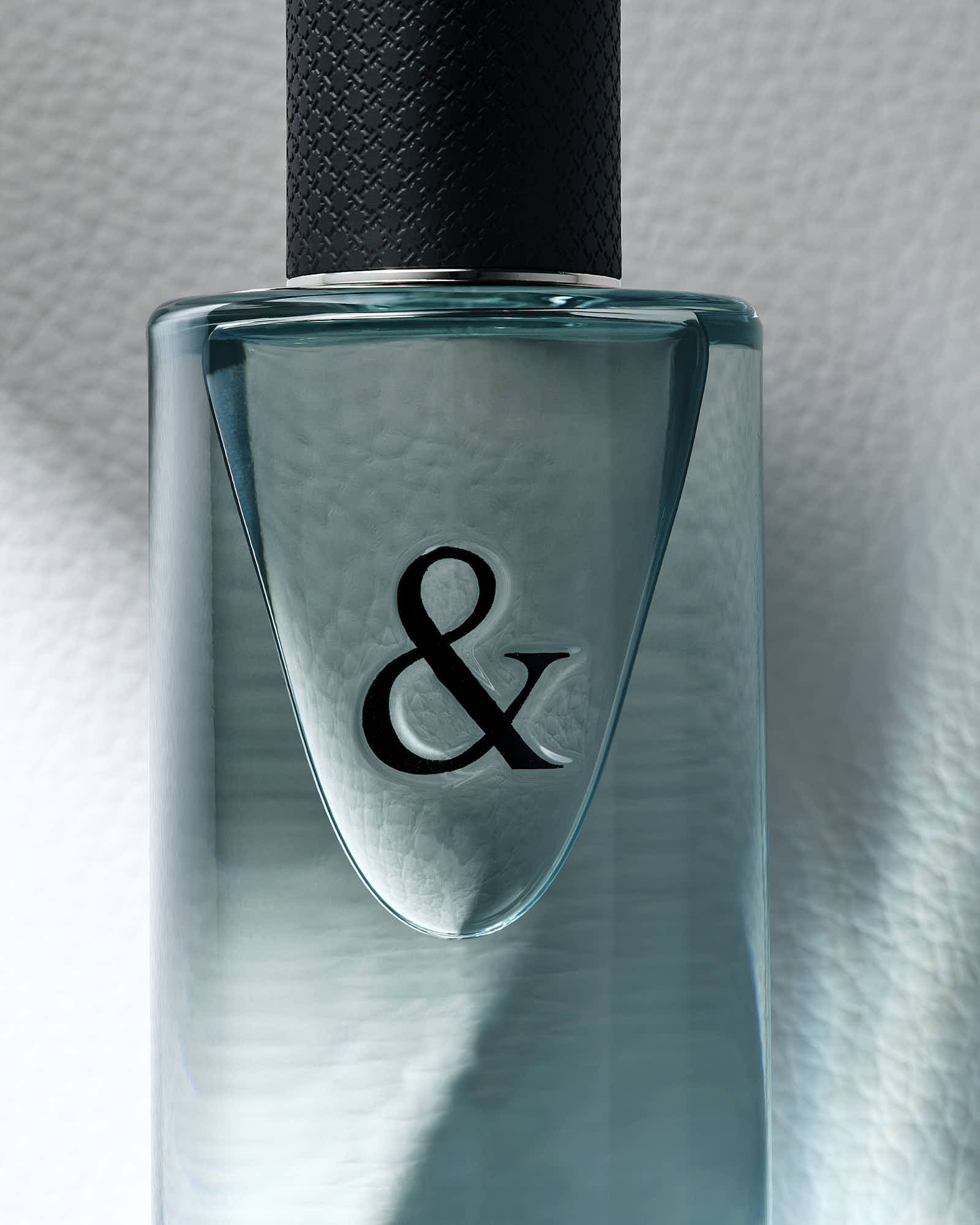 Elegant perfume bottle with textured cap and ampersand symbol, minimalist design.