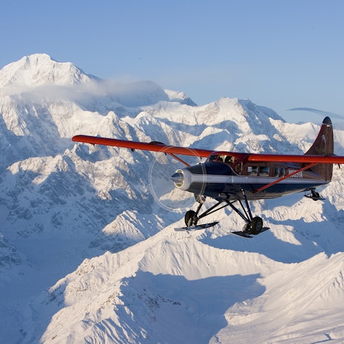 小型螺旋槳飛機，紅色的翅膀在清澈的藍天下飛越覆蓋著雪的山脈。