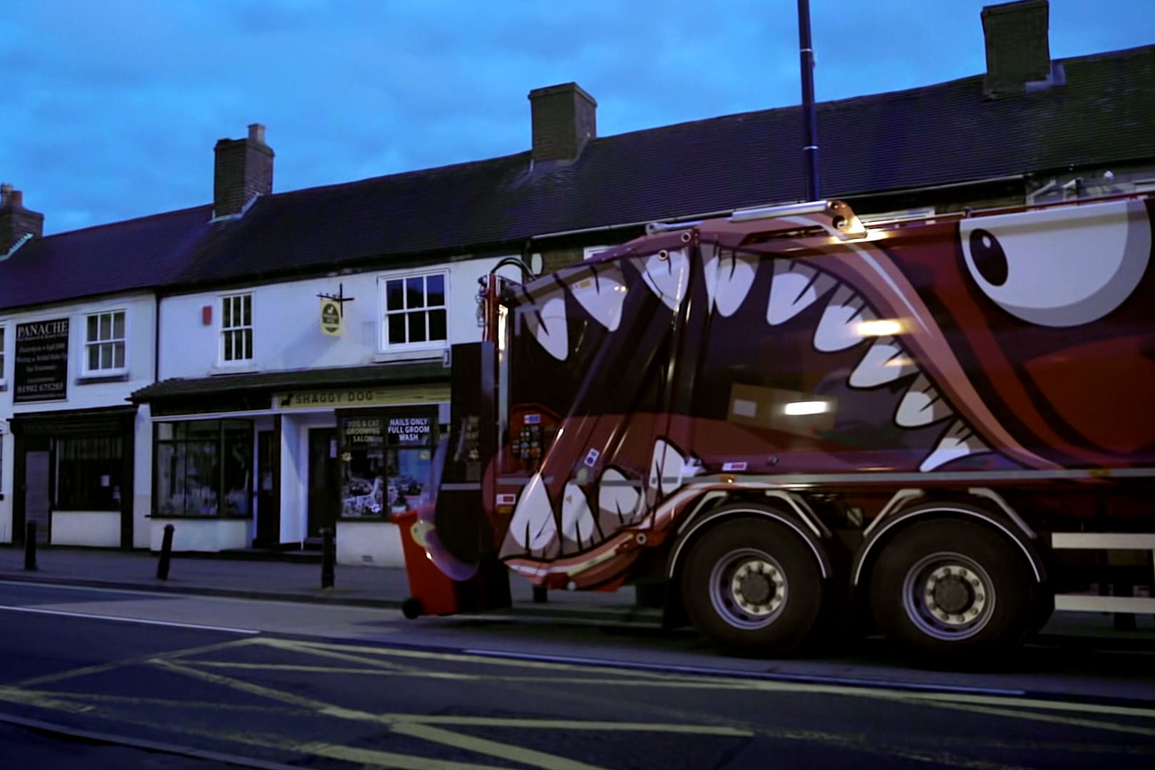 A garbage truck that has a illustrated monster drawn on it