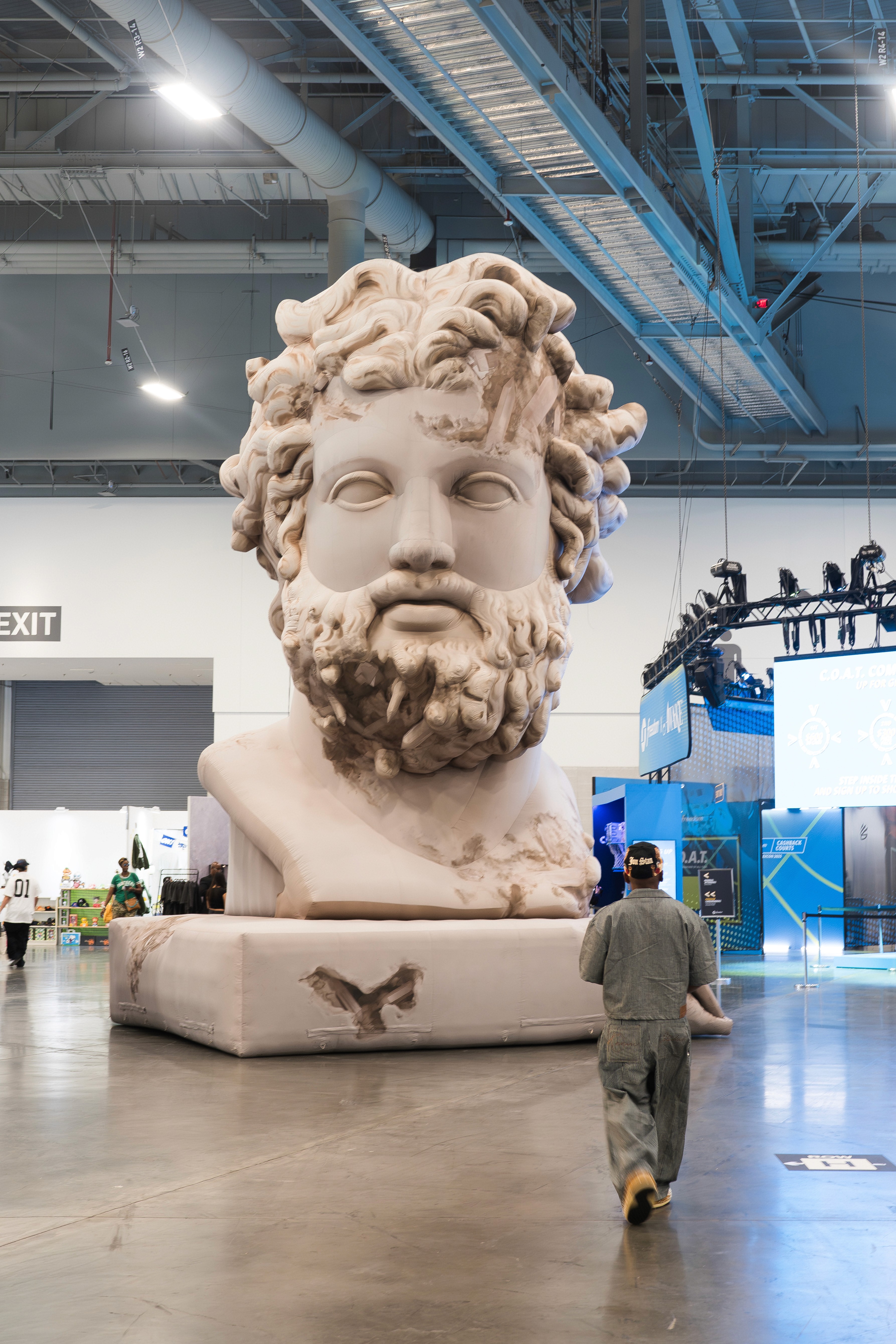 Person walking through an expo hall toward an oversized classical head sculpture installation.