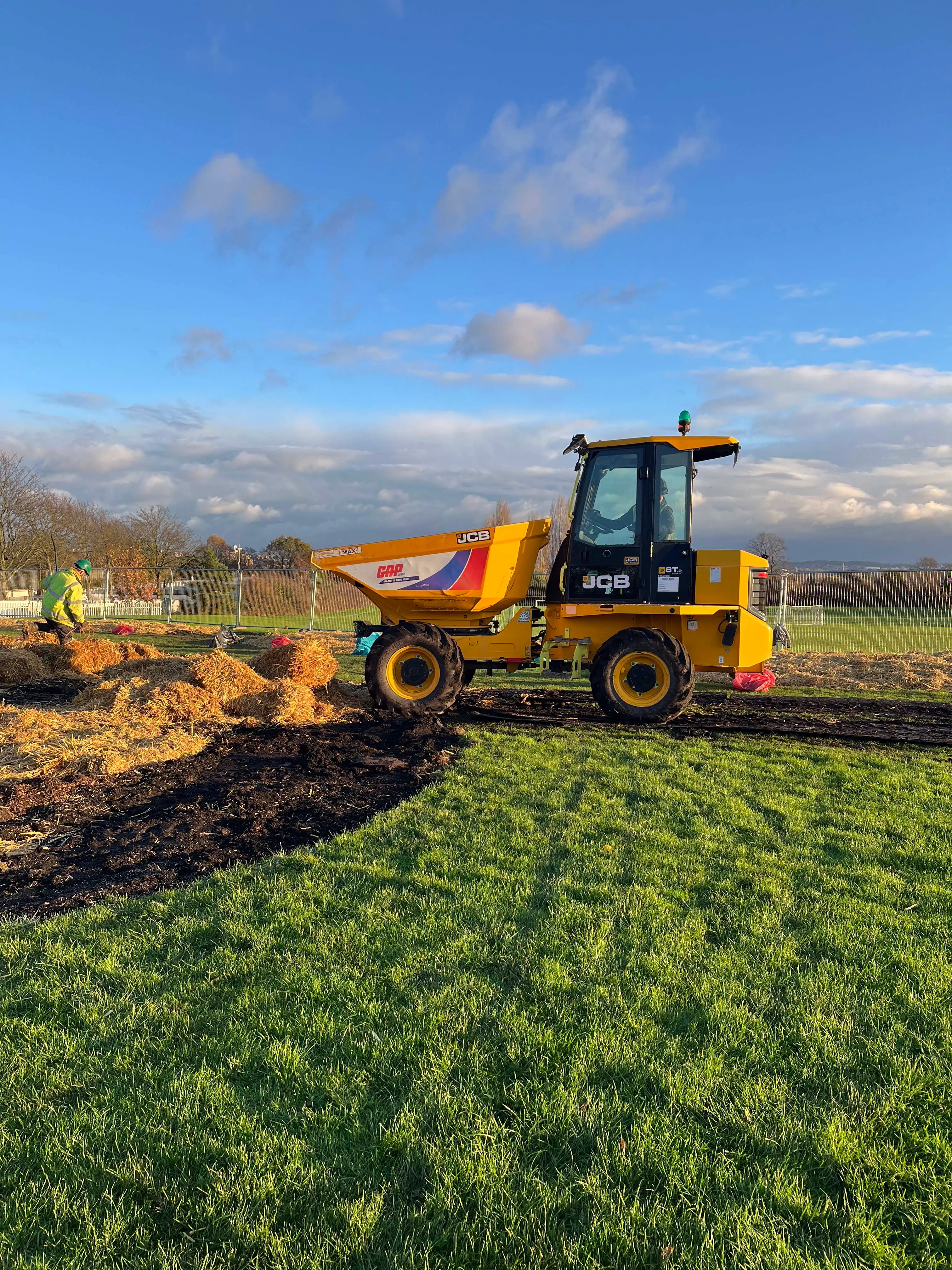 A yellow bulldozer is working on a field under a bright blue sky with some clouds in the background.